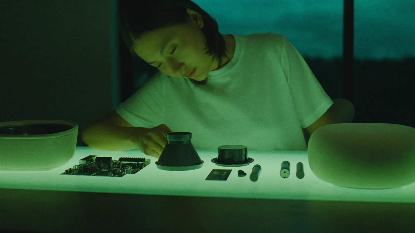 A product designer laying out the parts of a wireless speaker on a light table at night